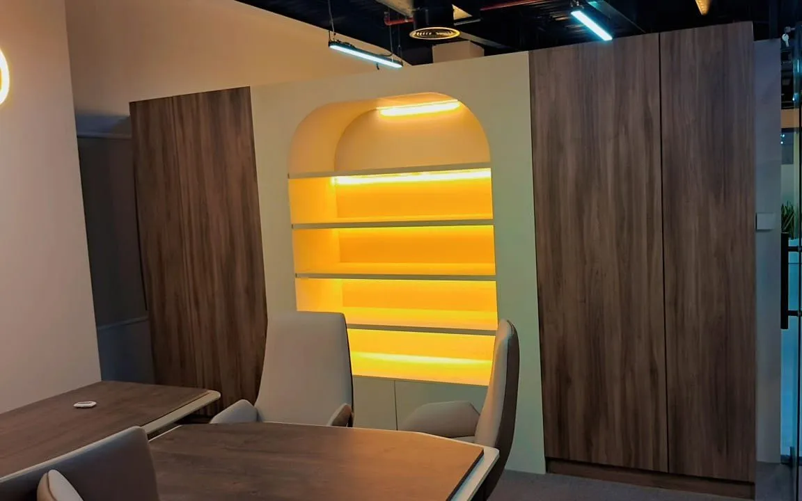 Breakout area with an arched backlit display niche between timber panelling and glass partitions