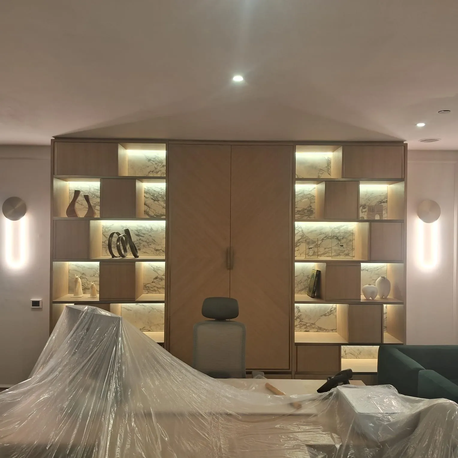 Backlit oak shelving wall with marble clad niches and a walnut wardrobe door