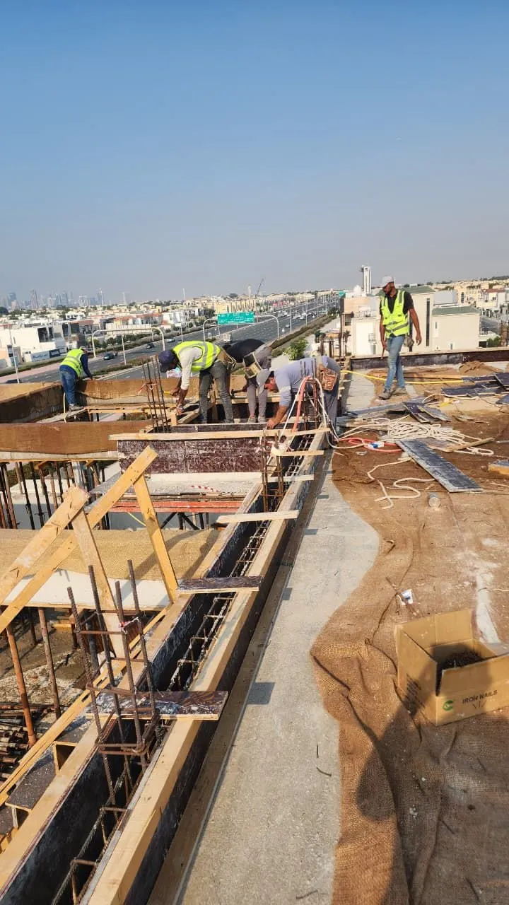 Five workers tying reinforcement along a rooftop parapet above a highway