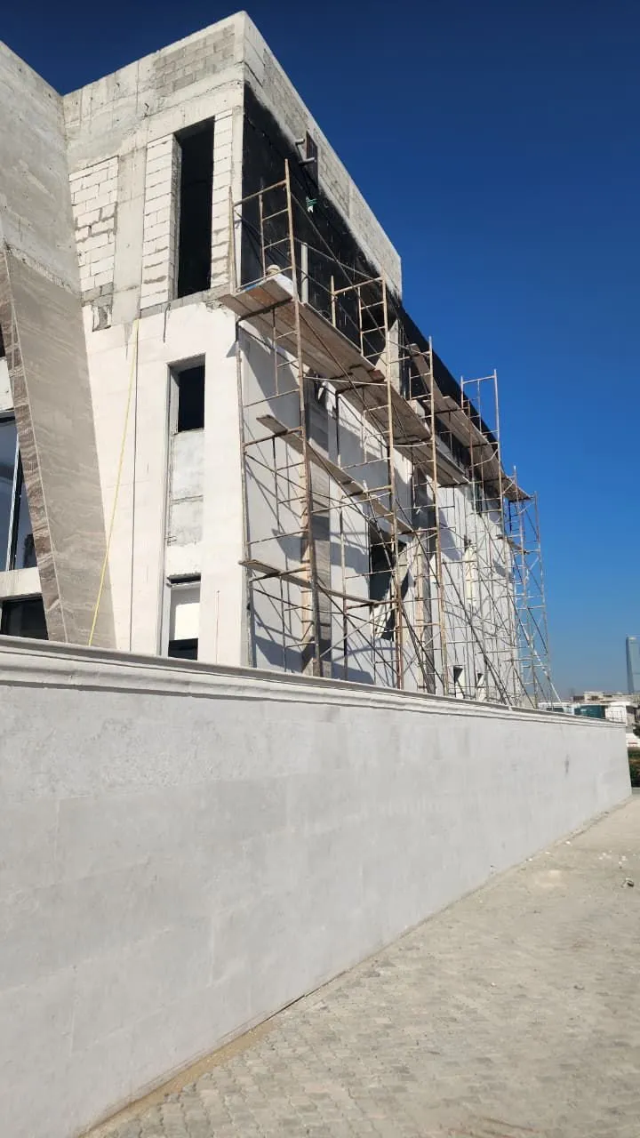 Near complete villa in stone cladding with tube scaffold and a worker at high level
